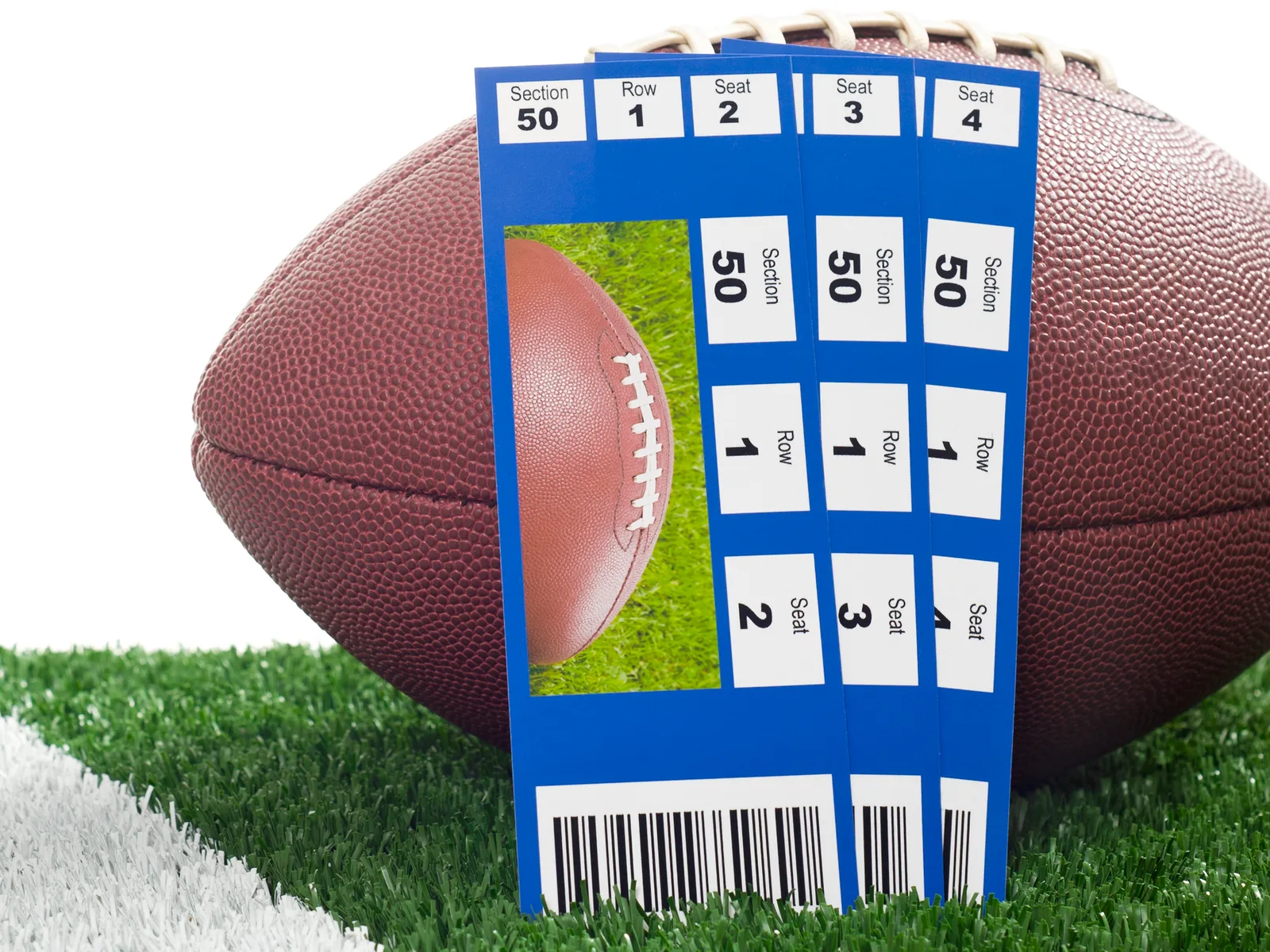 Two tickets propped against a football on the yard line of a field.